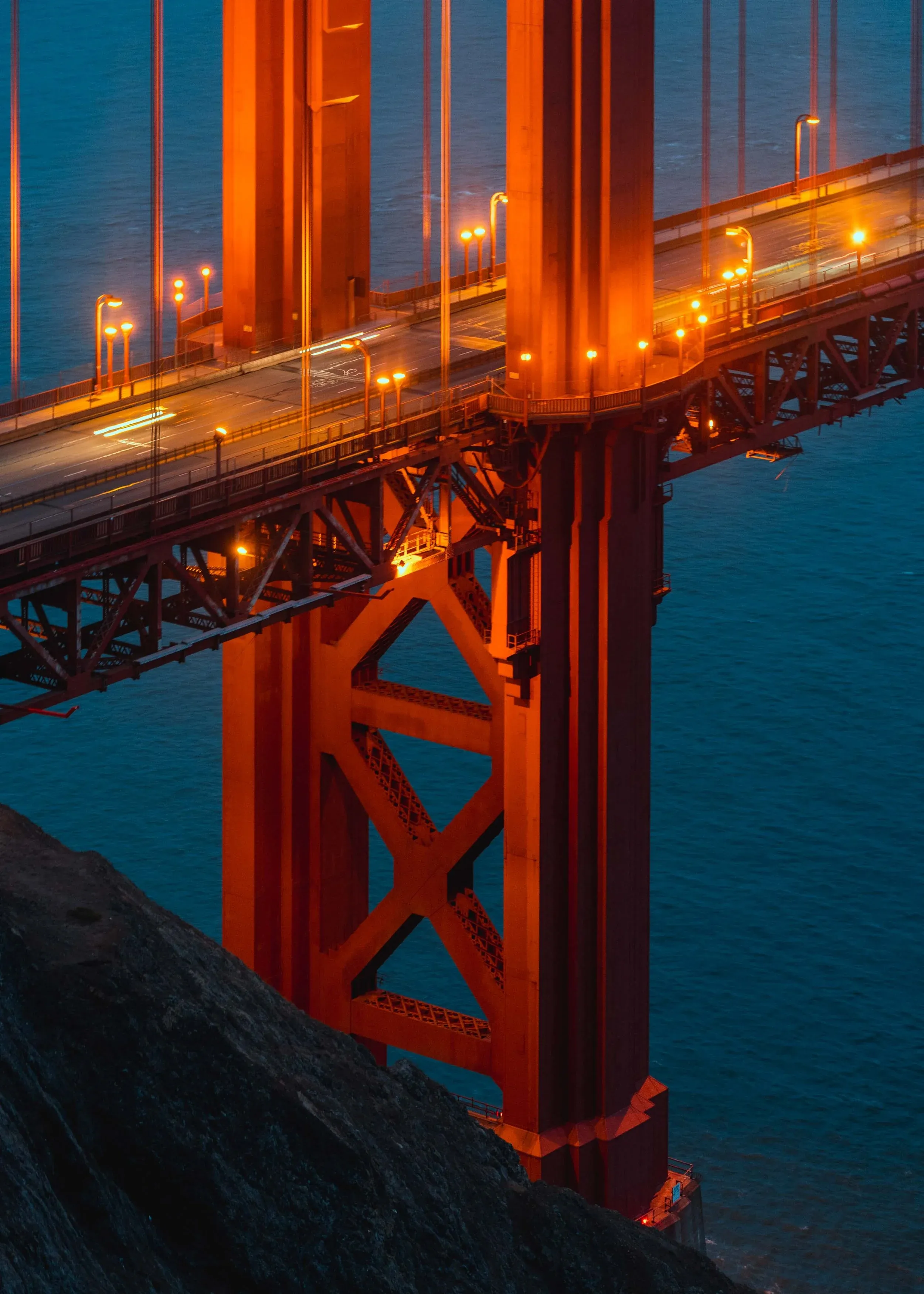 Golden Gate Bridge tower and roadway lit orange above dark blue water.