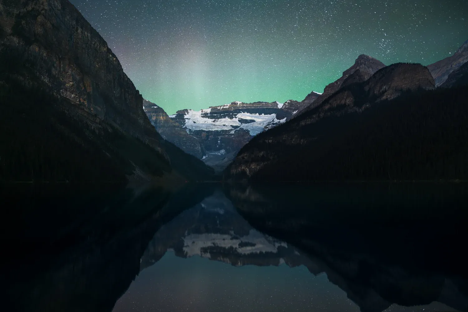Aurora over mountains reflected in a still lake at night.