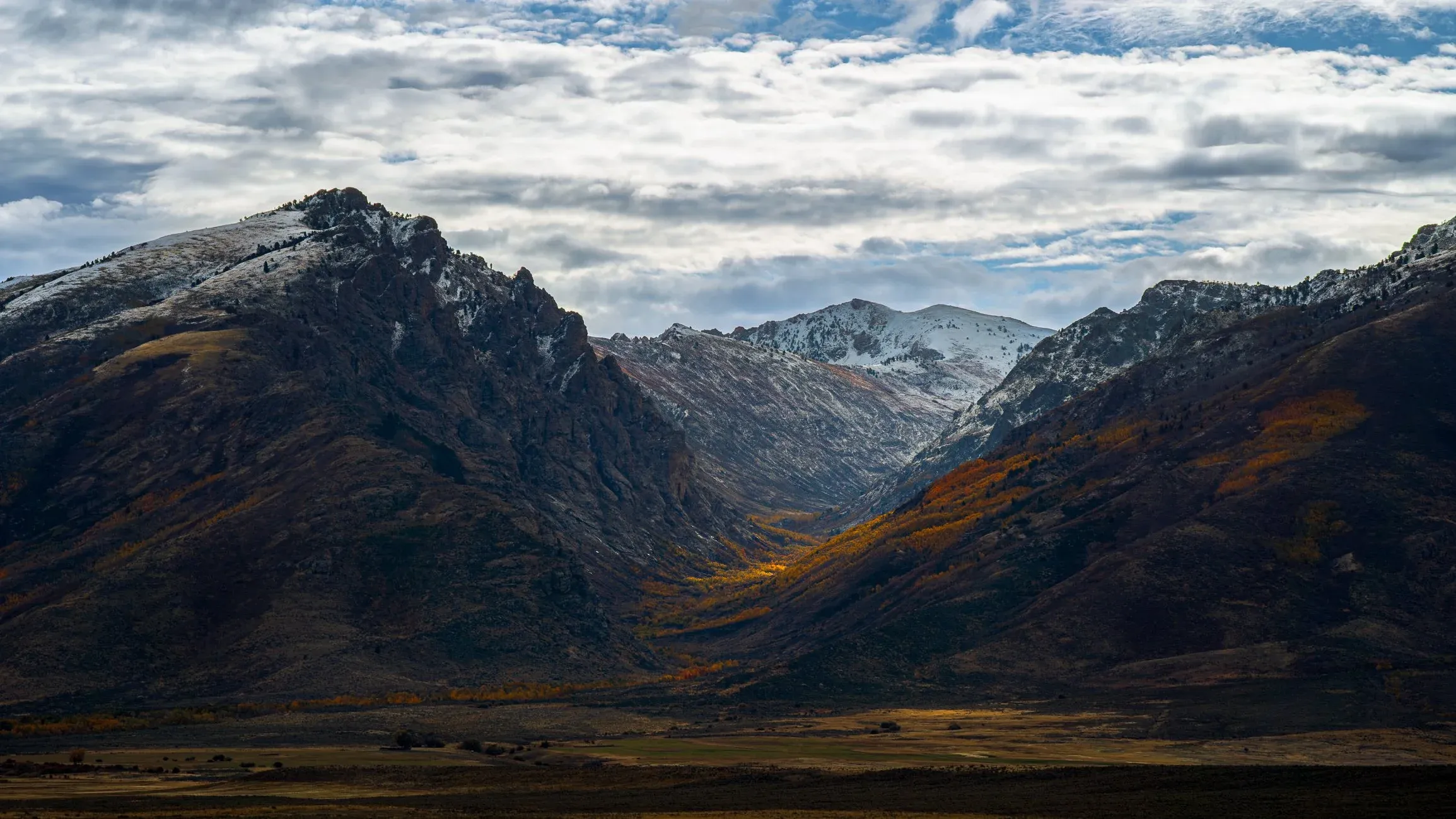 Rugged mountains under heavy cloud with warm light in the valley.