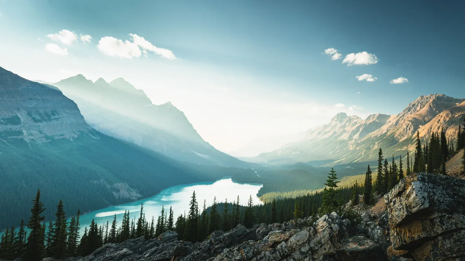 Turquoise glacial lake in a forested valley below hazy peaks.