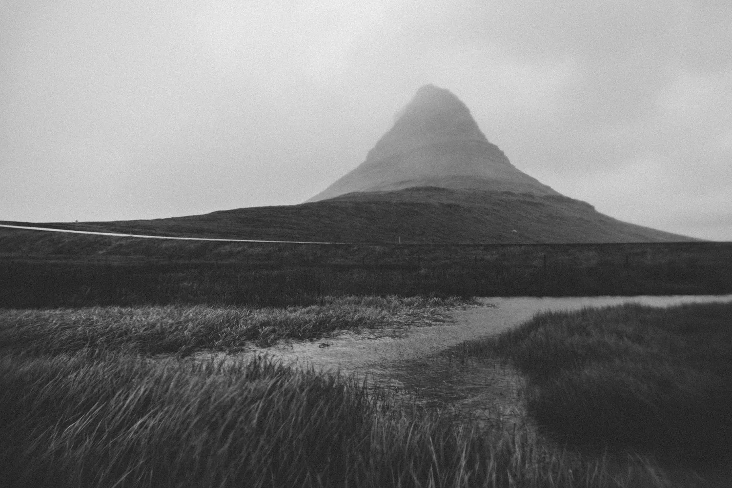 Black-and-white Kirkjufell mountain above grassland.