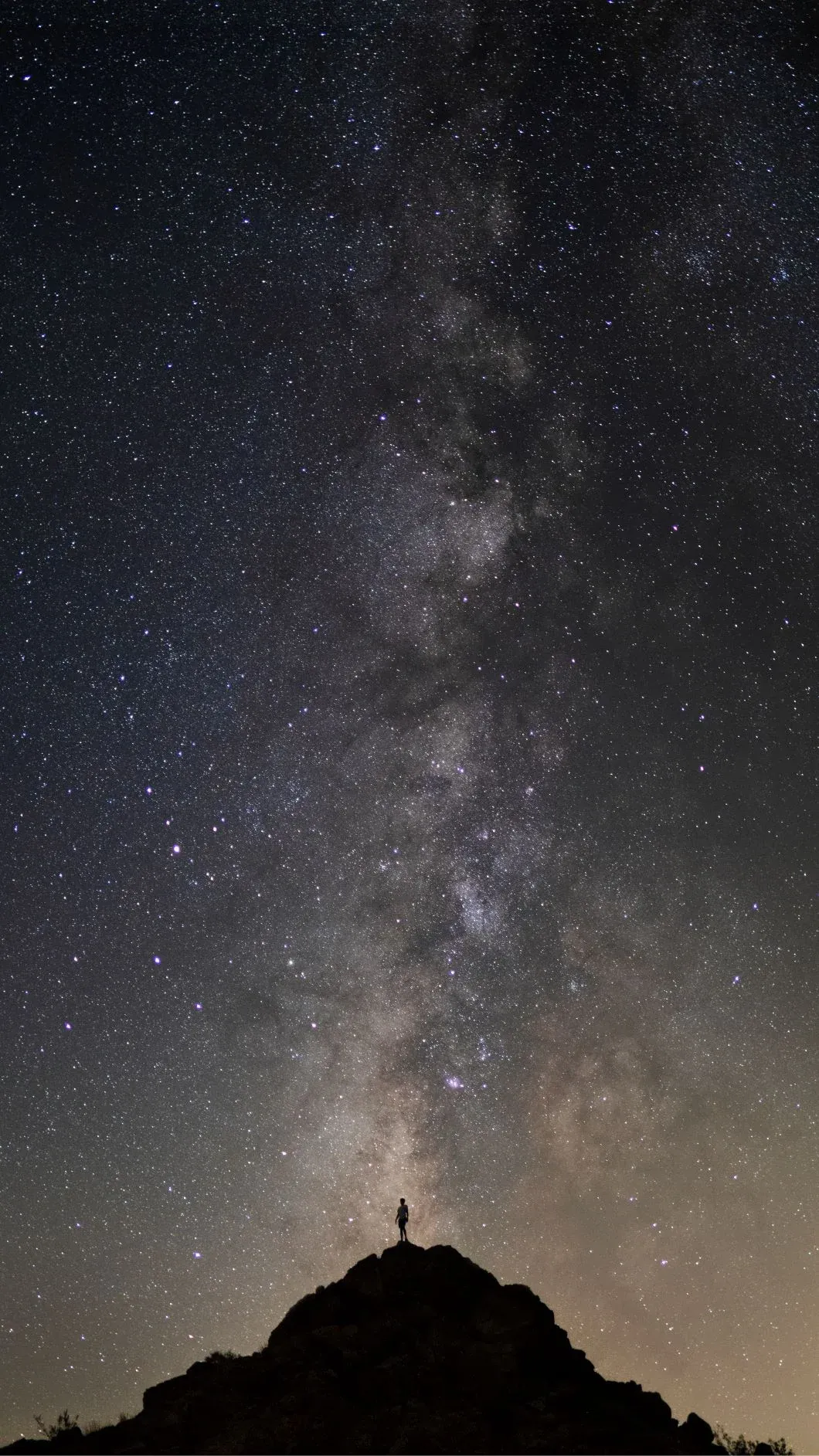 Milky Way rising over a lone figure on a rock.